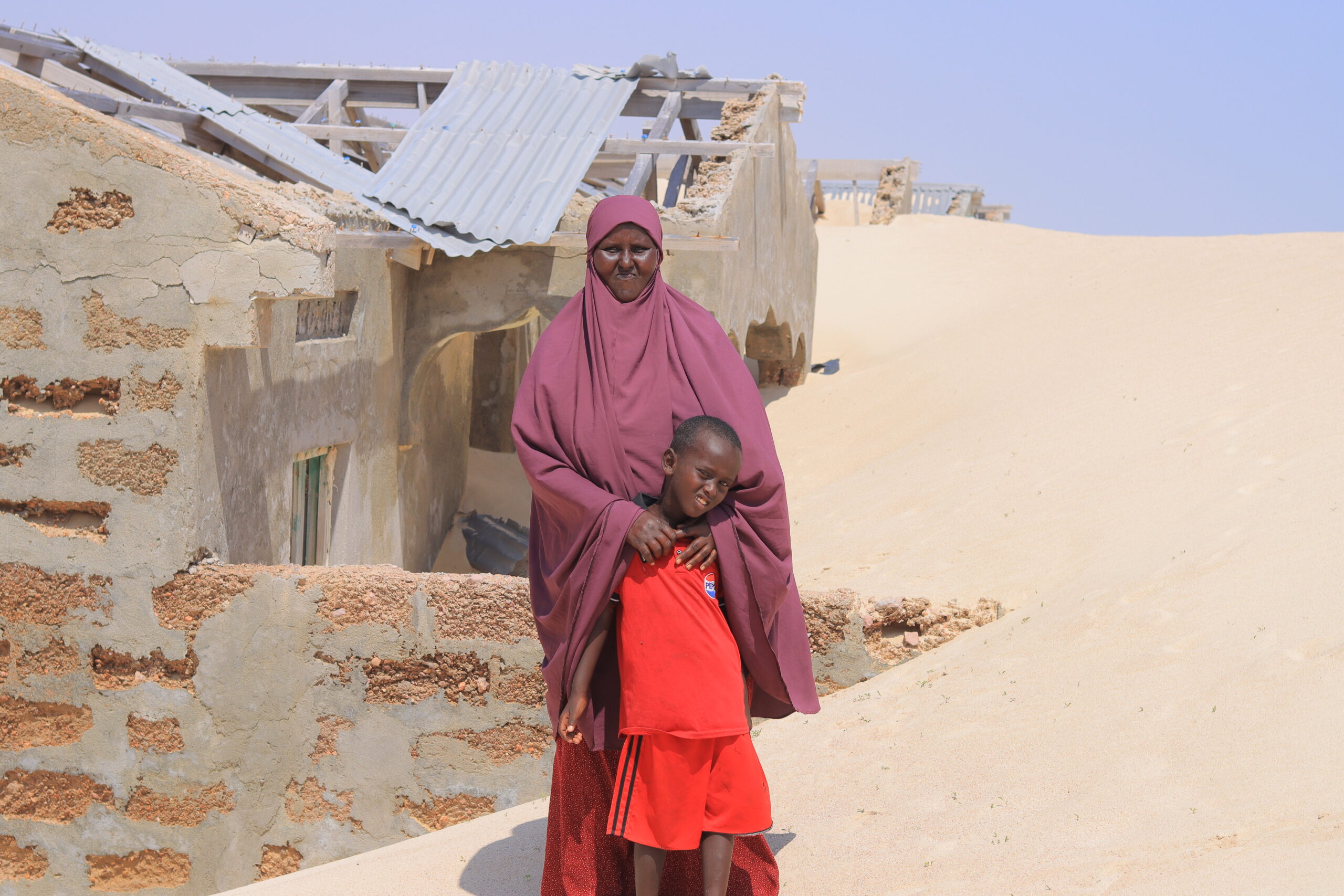 A Somali woman stands outside her sand-covered home in Kulub village, Mudug region, highlighting the impacts of climate change. | PHOTO/SAID ABDULLAHI KULMIYE.